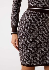 Hnedé pletené šaty s bielym geometrickým vzorom, rebrovanými manžetami a lemom s kontrastnými akcentmi. Priliehavý strih zvýrazňujúci siluetu.