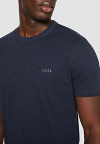 Námořnická modrá polo tričko s krátkým rukávem z jemné látky, s nenápadným šedým logem "BOSS" na hrudi a klasickým kulatým výstřihem.