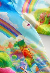 Tissu bleu brillant avec des arcs-en-ciel colorés, une planète, des nuages, des arbres vibrants, une rivière qui coule, et un petit lapin blanc près de l'ouverture d'une poche.