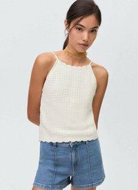 Bijeli teksturirani crop top s valovitim rubom i tankim naramenicama, uparen s trapericama. Tkanina ima uzorak rešetke.