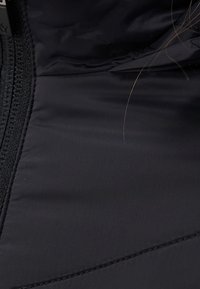 Interior de chaqueta acolchada negra con textura de tela lisa, detalles cosidos y cierre de cremallera a lo largo del borde.