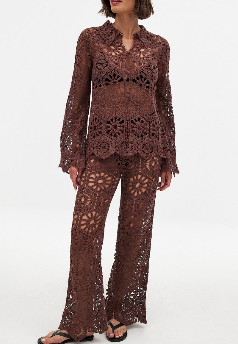 Brązowy, szydełkowany zestaw składający się z dwóch części, składający się z koszuli zapinanej na guziki w kwiatowe wzory oraz spodni o szerokich nogawkach. Przezroczysta struktura z misternym wzorem koronkowym.
