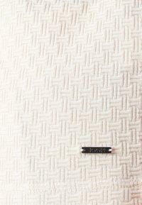 Tissu tricoté couleur crème présentant un motif géométrique texturé, avec une petite étiquette noire portant l'inscription "JOOP!" attachée.