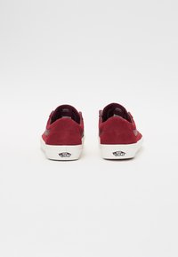 Røde ruskinds lavtop sneakers med hvide gummisåler og sorte logo detaljer. Har en polstret krave og kontrasterende sidelæbe design.