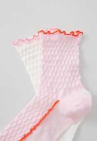 Pair of socks featuring a pink and white design. The pink sock has a honeycomb texture and ruffled edges with orange accents.