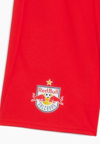 Camiseta deportiva roja de tela brillante con un escudo impreso que presenta dos toros rojos y un balón de fútbol, acentuado por una estrella encima del logotipo.