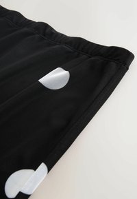 Zwarte stoffen shorts met een gladde textuur, voorzien van een groot wit halfcirkelpatroon aan de zijkant en een elastische tailleband.