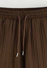 Pantalons en tissu plissé marron avec taille élastique et cordons de serrage marron dotés d'embouts en métal argenté.