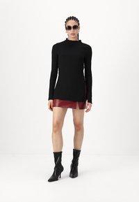 Black long-sleeve top with a high neckline, paired with a burgundy leather mini skirt and knee-high black heeled boots. Textured fabric details visible.