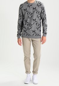 Sweat-shirt gris à col rond avec motif de feuilles noires, associé à un pantalon beige retroussé et des baskets blanches. Coupe décontractée et tissu léger.