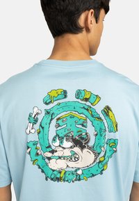 Light blue t-shirt featuring a colorful graphic of a cartoon wolf surrounded by circular designs and bones, printed on the back.