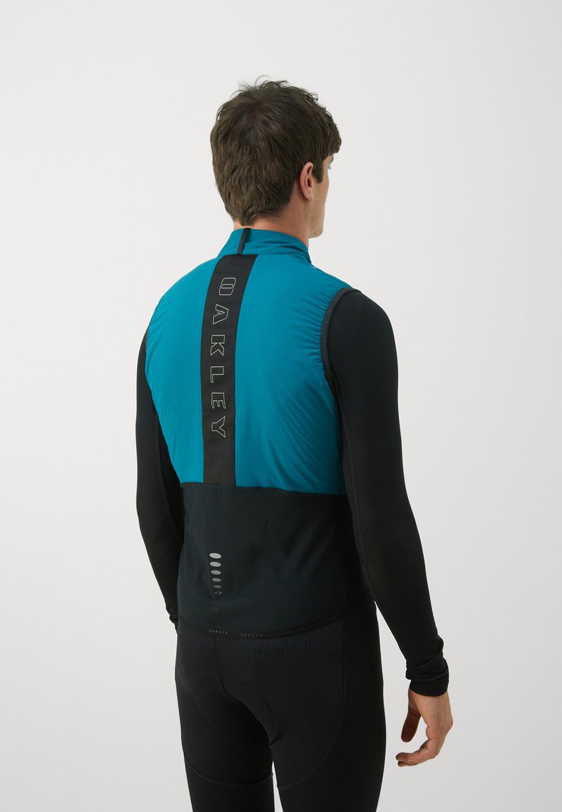 Herren-Radsportweste mit teal-farbener Vorderseite, schwarzer Rückseite und reflektierenden Akzenten. Das Material ist glatt, hat eine taillierte Passform und einen hohen Kragen.