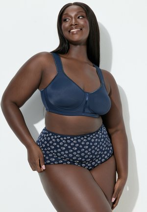 Laivastonsininen urheiluliivi leveillä olkaimilla ja edessä oleva lukko; yhdistetty korkeavyötäröisiin alushousuihin, joissa on valkoinen kukkakuvio. Sileä pinta.