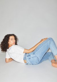 Jeans en denim bleu clair au design ajusté et à l'effet délavé subtil, associés à un t-shirt blanc uni, sur un fond neutre.