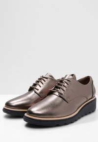 Metalen bronzen veterlaarzen met een glad leren afwerking, voorzien van een verhoogde zwarte rubberen zool en subtiele stiksel details.