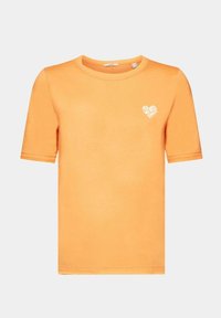 T-shirt orange en coton doux, avec un col rond et des manches courtes. Il présente un petit graphisme de cœur blanc avec du texte sur le devant.