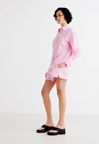 Rosa stripete skjorte med lange ermer, kombinert med matchende shorts. Bært med svarte sandaler i en kraftig design.