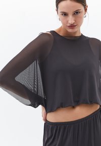 Svart genomskinlig kort topp med korta vida ärmar, lätt material och avslappnad passform, som matchas med byxor med mörk elastisk midja.