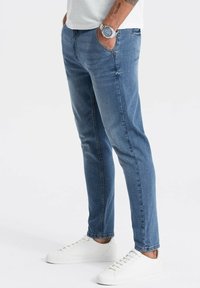 Ljusblå denimjeans med slim fit, femficksdesign och subtila slitage detaljer. Kombinerat med vita sneakers och en armbandsklocka.