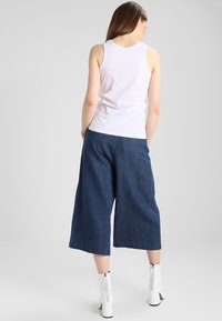 Biała bezrękawnikowa bluzka zestawiona z szerokimi, ciemnoniebieskimi dżinsowymi kulotami. Ubranie charakteryzuje się luźnym krojem i minimalistycznym designem.