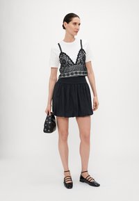 Čierny čipkový bralette cez biely tričko, doplnený čiernou sukňou. Doplnky tvoria malá čierna taška a čierne ploché topánky so strapcami.