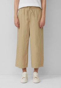 Beige wijde broek gemaakt van lichtgewicht stof met een elastische tailleband en trekkoord. Gecombineerd met witte sneakers.