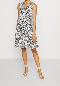 Bílá šaty bez rukávů s leopardím potiskem, výstřihem do V, volánkovým lemem a lehkým materiálem. Kombinováno s bílými sandály na řemínky.