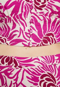 Kukkakuvioinen crop top, jossa on vaaleanpunainen ja valkoinen kangas suurilla kukkakuvioilla. Etuosassa on napit ja sileä pinta.