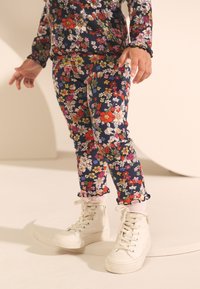 Marinblå klädset med blommönster och volangkanter, kombinerat med vita sneakers med hög ankel. Har livfulla blommor i blått, rött och grönt.