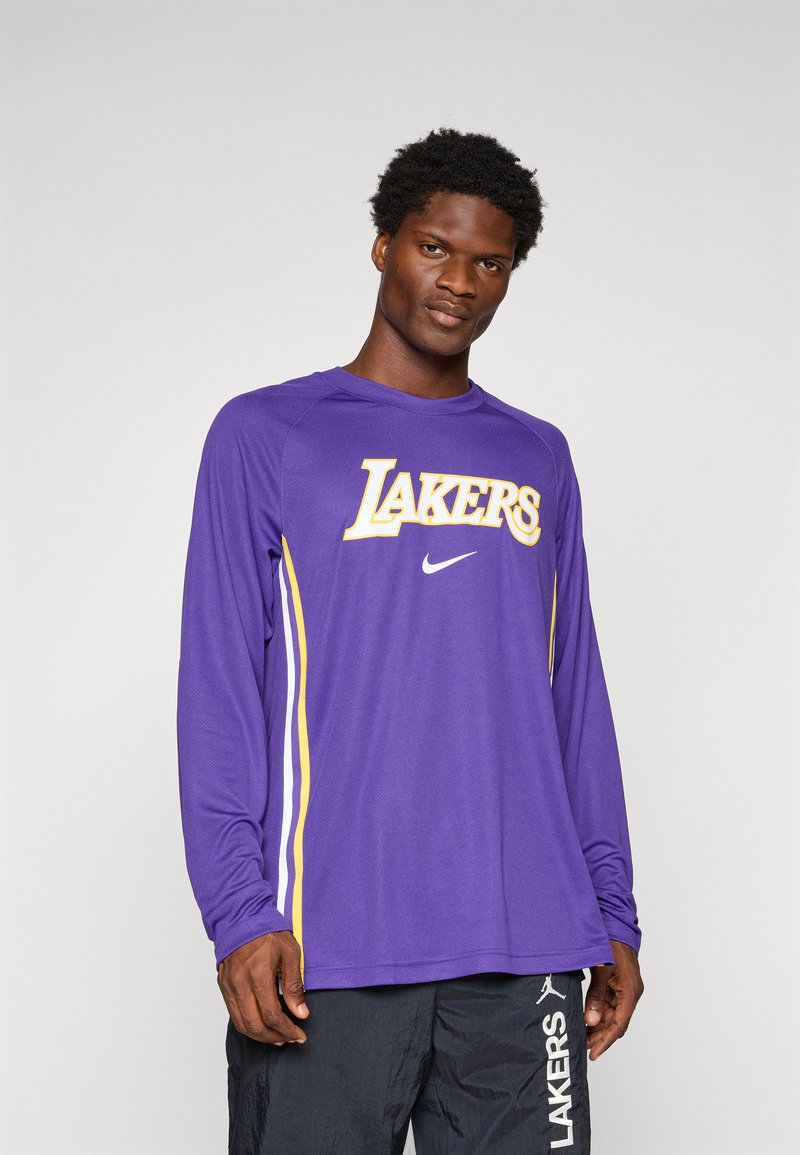 Chemise à manches longues violette avec le logo "LAKERS" en jaune, présentant des bandes latérales blanches. Le matériau semble léger et respirant.