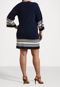 Laivaston sininen neulemekko, jossa on kolmanneksi viimeiset hihat, ja jotka on varustettu valkoisilla ja beigellä raidallisilla yksityiskohdilla hihoissa ja helmassa. Vartalonmyötäinen malli.