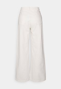 Leveled trousers dalam campuran katun berwarna putih kekuningan, dengan pinggang tinggi, dua saku belakang, dan permukaan yang halus serta bertekstur.