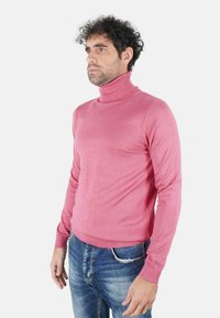 Maglione a dolcevita rosa realizzato in tessuto a maglia liscia, con collo e polsini a coste, abbinato a jeans blu strappati.