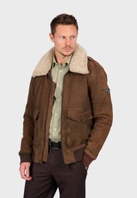 Giacca in pelle marrone con colletto in shearling, chiusura lampo, due tasche anteriori, polsini a costine, finitura testurizzata e una toppa ricamata sulla manica.