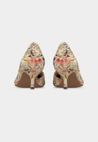 Paire d'escarpins beige à motif floral pour femme avec des talons aiguilles fins de hauteur moyenne, vus de dos sur fond blanc.