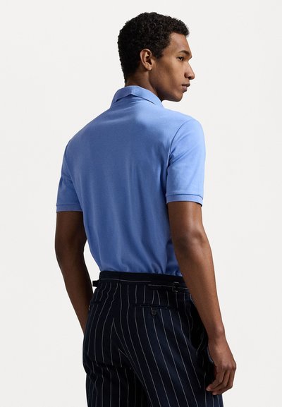 Camisa polo de manga corta azul claro con una textura suave, combinada con pantalones oscuros de rayas finas. El cuello es clásico y está plano.