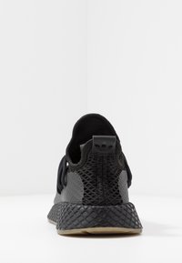Svart sportskor med en vävd meshöverdel, släta läderdetaljer, texturerad häl och gummisulor. Har en diskret logotyp på baksidan.