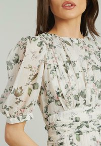 Blumenkleid aus leichtem Stoff mit sanften Pastellfarben, puffärmeligen Ärmeln, vertikalen Falten und einer taillierten Taille mit floralen Mustern.