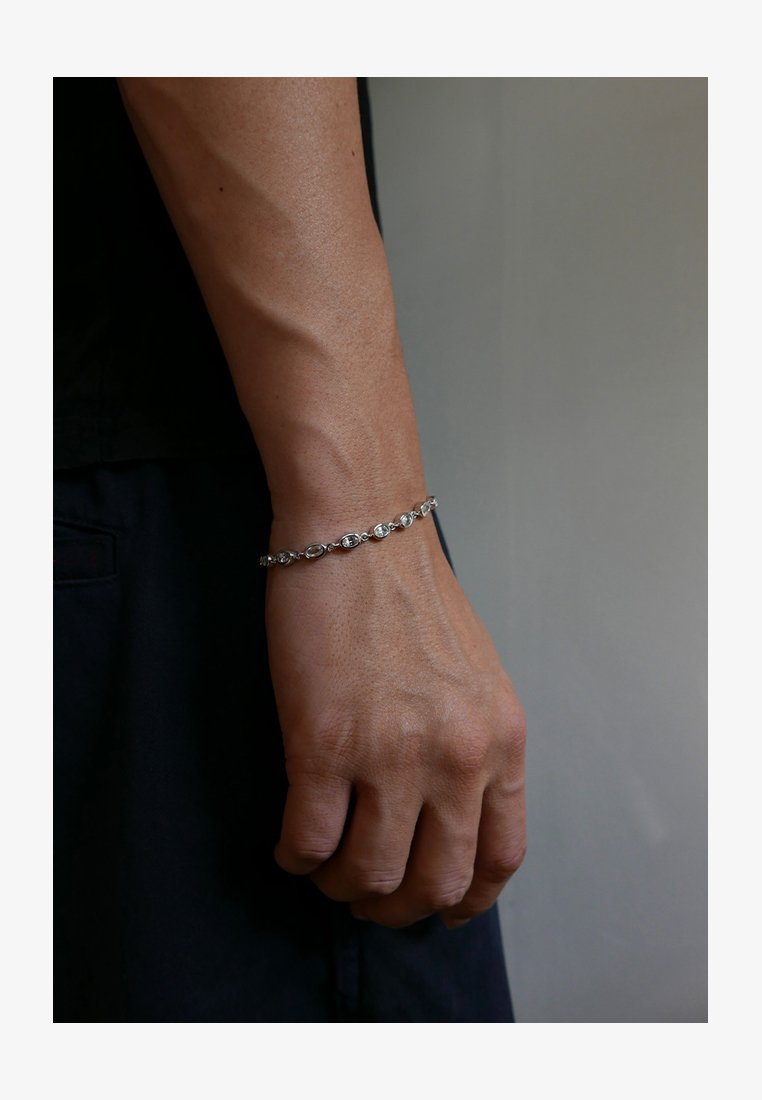 Silver bracelet with oval links, featuring small circular accents. Worn on a wrist with visible veins and a textured skin surface.