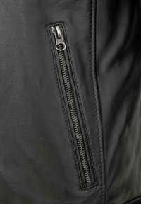 Schwarze Lederjacke mit Nahaufnahme eines silbernen Reißverschlusses, der eine strukturierte Oberfläche und saubere Nähte an den Kanten zeigt.
