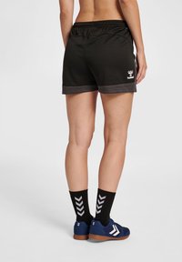 Svarta sportshorts med en texturerad yta, med en grå kant och hummel-logotyp. Kombinerat med marinblå skor och svarta strumpor med vita chevrons.
