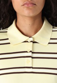 Polo shirt in lichtgeel met bruin en witte horizontale strepen, met een kraag en drie knoopsluitingen. Getextureerde stof.