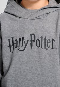Felpa grigia con cappuccio, caratterizzata da un logo "Harry Potter" nero in un carattere stilizzato. Tessuto morbido con un cappuccio ampio e polsini a costine.