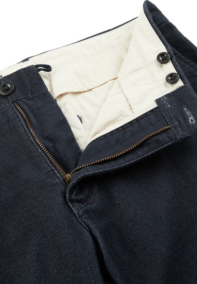 Pantalones de mezclilla azul marino con cremallera, un cierre metálico, dos botones en la cintura y un forro interior color crema.