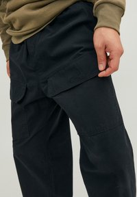Pantaloni cargo neri con tasche laterali, realizzati in tessuto leggero. Presentano una vestibilità comoda e cuciture visibili sulle tasche.