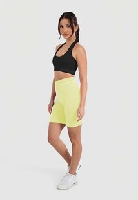 Czarny sportowy stanik na ramiączkach typu racerback i żółte krótkie spodenki rowerowe z wysokim stanem, ozdobione akcentami z logo i wykonane z gładkiego, elastycznego materiału.