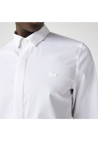 Camisa blanca de botones con un cuello clásico y un pequeño logo bordado. Tejido suave con un ajuste estructurado y detalles mínimos.