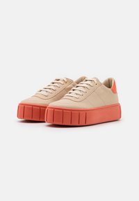 Des sneakers beiges avec une tige en cuir texturé, dotées d'une semelle intermédiaire corail, d'un bout rond et d'un laçage standard. Détails dorés au niveau des œillets.