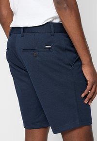 Navyblaue Shorts aus einem strukturierten Stoff, mit einer Gesäßtasche mit Knopfverschluss und einem kleinen Markenetikett.