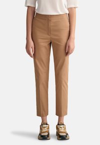 Brown, tailored ankle-length pants with a smooth texture and a fitted design, paired with multi-colored sneakers.